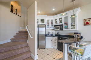 Kitchen with freestanding refrigerator, dark countertops, white cabinetry, dishwashing machine, and pendant lighting