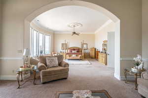 Living room with arched walkways, carpet floors, ornamental molding, and ceiling fan