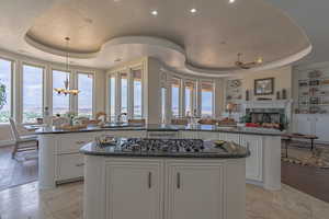 Kitchen with gas stovetop, a tray ceiling, a center island, built in shelves, and a ceiling fan