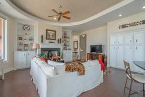 Living area with ceiling fan, dark wood-type flooring, built in shelves, a fireplace, and recessed lighting