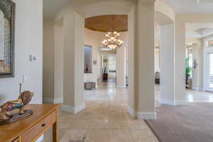 Corridor featuring arched walkways, a chandelier, ornate columns, and light carpet