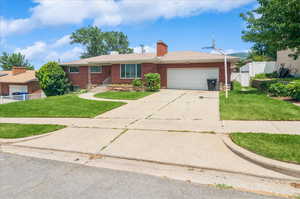 Ranch-style home featuring an attached garage, brick siding, driveway, and a chimney
