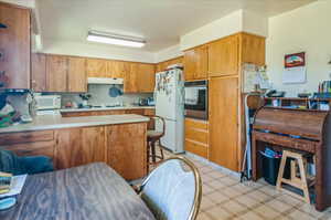 Kitchen featuring white appliances, light countertops, under cabinet range hood, a peninsula, and brown cabinets