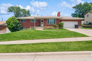 Single story home with an attached garage, concrete driveway, brick siding, a chimney, and a front lawn