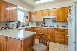 Kitchen with white appliances, under cabinet range hood, light countertops, and a peninsula