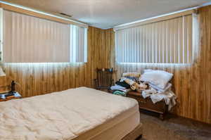 Bedroom featuring a textured ceiling, wooden walls, and carpet floors