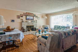 Living area featuring a textured ceiling, wood finished floors, crown molding, and a fireplace