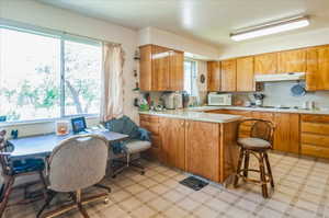 Kitchen with white appliances, under cabinet range hood, light countertops, a peninsula, and brown cabinetry