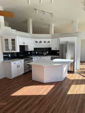 Kitchen featuring white cabinets, tasteful backsplash, glass insert cabinets, stainless steel appliances, and a center island