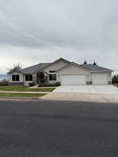 Ranch-style home featuring stone siding, concrete driveway, roof with shingles, and a front yard
