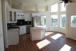 Kitchen with glass insert cabinets, decorative backsplash, white cabinetry, a center island, and stainless steel appliances