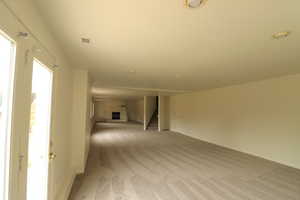 Unfurnished living room featuring light colored carpet, stairs, a fireplace with raised hearth, and recessed lighting