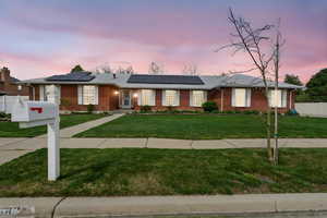 Ranch-style house featuring roof mounted solar panels and brick siding