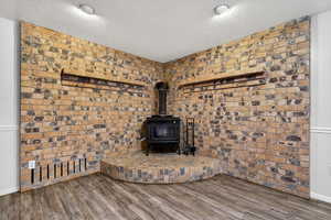 Detailed view of a wood stove, wood finished floors, and exposed brick.