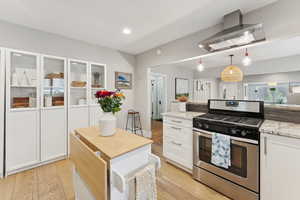 Kitchen featuring stainless steel gas range, wall chimney exhaust hood, white cabinetry, light wood finished floors, and recessed lighting