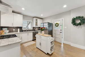 Kitchen featuring appliances with stainless steel finishes, backsplash, light wood-type flooring, open shelves, and white cabinetry