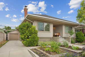 View of front of house featuring a garden, driveway, a chimney, a garage, and an outdoor structure