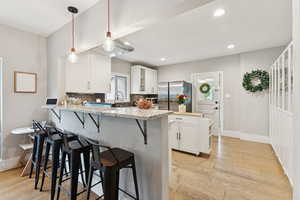 Kitchen featuring freestanding refrigerator, a breakfast bar area, a peninsula, white cabinets, and light wood-type flooring