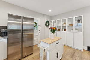 Kitchen with stainless steel refrigerator, light wood-style flooring, white cabinetry, butcher block countertops, and recessed lighting