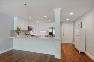 Kitchen featuring stainless steel appliances, a peninsula, light countertops, dark wood-style floors, and recessed lighting