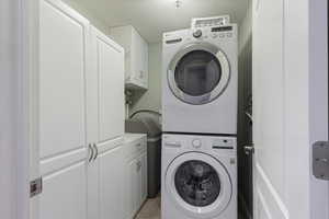 Laundry area featuring stacked washing machine and dryer, cabinet space, a textured ceiling, and light tile patterned flooring