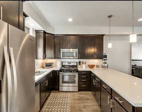 Kitchen with stainless steel appliances, dark brown cabinets, pendant lighting, light wood finished floors, and recessed lighting