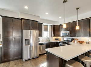 Kitchen with dark brown cabinetry, a kitchen breakfast bar, appliances with stainless steel finishes, a peninsula, and hanging light fixtures