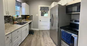 Kitchen with appliances with stainless steel finishes, light wood finished floors, backsplash, white cabinets, and light stone countertops