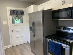 Kitchen with stainless steel appliances, light wood-type flooring, and white cabinetry