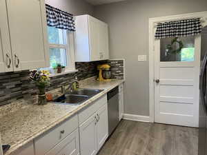 Kitchen featuring stainless steel dishwasher, dark wood-style floors, backsplash, white cabinetry, and freestanding refrigerator