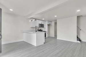Kitchen with stainless steel appliances, white cabinetry, light countertops, light wood finished floors, and open floor plan