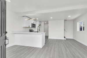 Kitchen with stainless steel microwave, light wood finished floors, light countertops, a peninsula, and recessed lighting