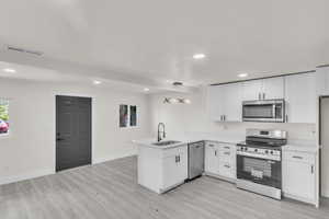 Kitchen featuring appliances with stainless steel finishes, a peninsula, light wood finished floors, recessed lighting, and white cabinets
