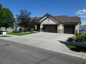 View of front facade with an attached garage, concrete driveway, stone siding, and a front yard