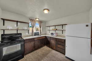Kitchen featuring open shelves, freestanding refrigerator, black range with electric cooktop, dark brown cabinetry, and a textured ceiling