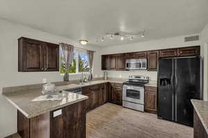 Kitchen with stainless steel appliances, dark brown cabinetry, a peninsula, and light wood-style flooring