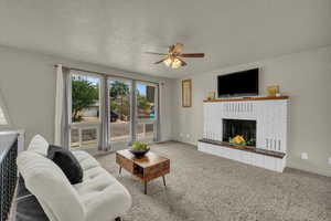 Carpeted living room featuring a fireplace and ceiling fan