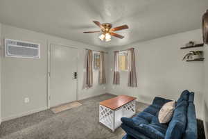 Carpeted living area with an AC wall unit, a ceiling fan, and a textured ceiling
