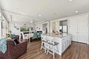 Kitchen featuring stainless steel fridge, open floor plan, wood finished floors, white cabinetry, and recessed lighting