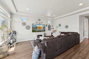 Living area with a raised ceiling, wood finished floors, recessed lighting, and a warm lit fireplace