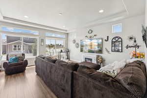 Living area featuring a raised ceiling, hardwood / wood-style floors, a glass covered fireplace, and recessed lighting