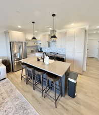 Kitchen featuring appliances with stainless steel finishes, tasteful backsplash, hanging light fixtures, an island with sink, and open shelves