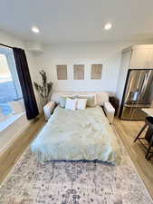 Bedroom with stainless steel fridge, light wood-type flooring, and recessed lighting