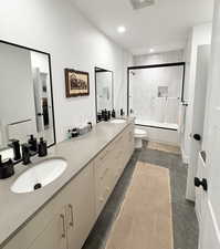 Full bathroom with double vanity, dark tile patterned flooring, combined bath / shower with glass door, and recessed lighting