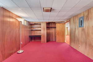 Unfurnished bedroom featuring carpet floors, wooden walls, electric panel, and a closet