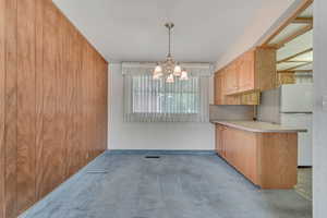 Kitchen featuring freestanding refrigerator, a chandelier, carpet floors, light countertops, and a peninsula