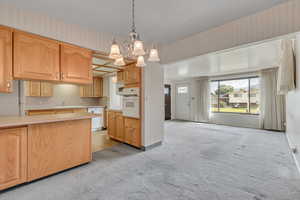 Kitchen featuring white appliances, a chandelier, wallpapered walls, light carpet, and light countertops