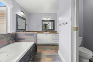 Full bathroom with stone tile floors, a bath, and vanity
