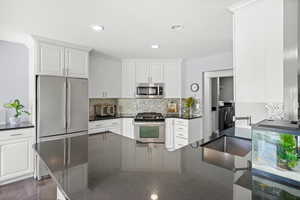 Kitchen with appliances with stainless steel finishes, washing machine and dryer, white cabinets, tasteful backsplash, and recessed lighting
