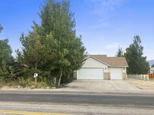 View of property hidden behind natural elements featuring brick siding, an attached garage, and concrete driveway